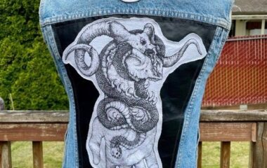 Ljusblå denimväst med svart ryggpanel, drakmotiv och rund symbol