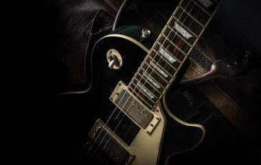Närbild av en svart elgitarr med dubbla humbuckers i mörkt ljus
