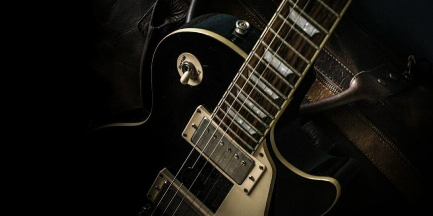 Närbild av en svart elgitarr med dubbla humbuckers i mörkt ljus